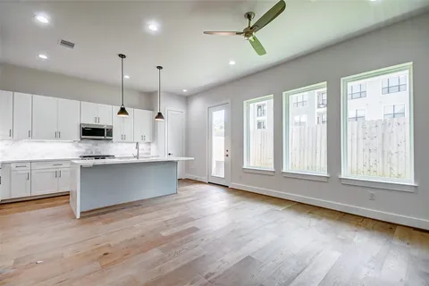 a large kitchen with stainless steel appliances kitchen island granite countertop a stove a sink and white cabinets with wooden floor