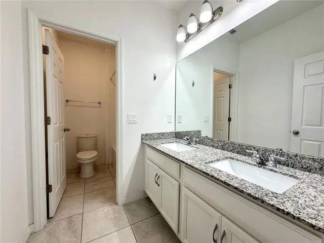 a spacious bathroom with a granite countertop sink a toilet and a large mirror