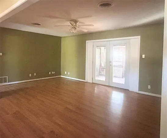 an empty room with wooden floor and windows with curtains