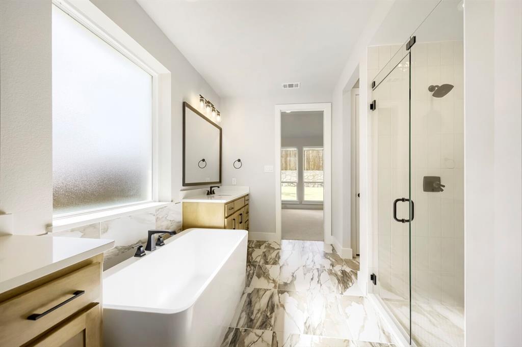 800 Blackberry Road Haslet, TX 76052 - Photo 22 of 28 Contemporary bathroom featuring a freestanding soaking tub, a frameless glass shower enclosure, a dual-sink vanity with wood-finish cabinetry, a large rectangular mirror, and marbled tile flooring