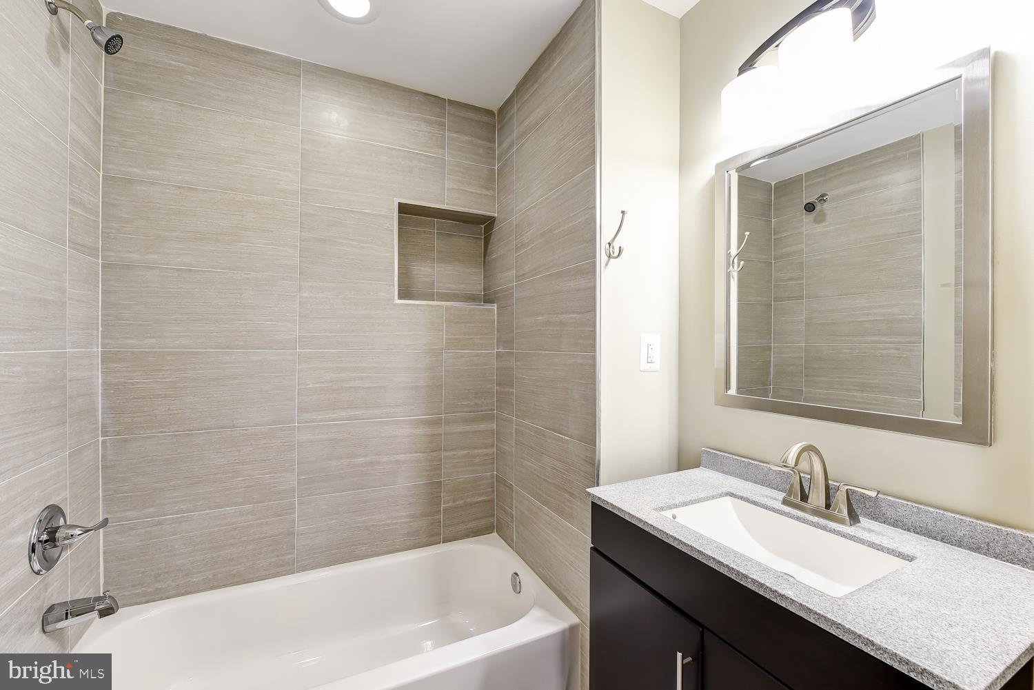 2031 Benning Road Northeast, Unit B Washington, DC 20002 - Photo 10 of 22 a bathroom with a granite countertop sink a mirror a bathtub and shower