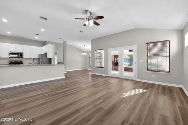 a view of an empty room and kitchen with wooden floor and a ceiling fan