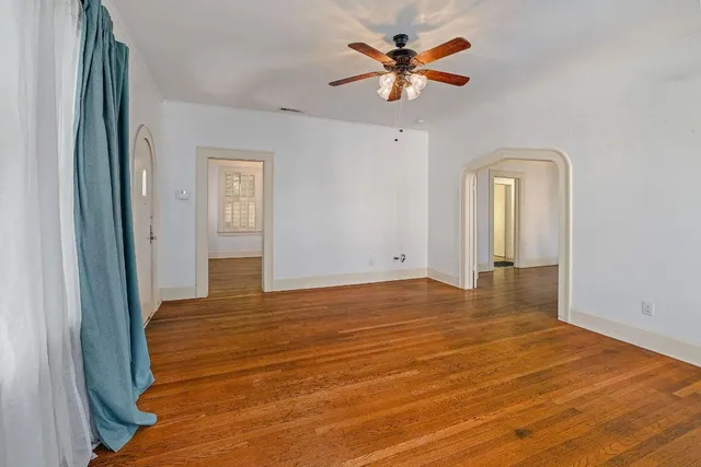 a view of an empty room with wooden floor and a ceiling fan
