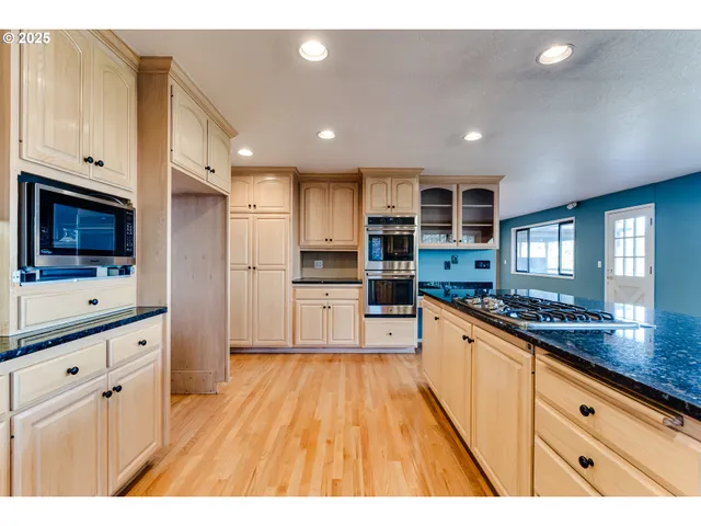 a kitchen with stainless steel appliances kitchen island granite countertop a stove a sink dishwasher and white cabinets with wooden floor