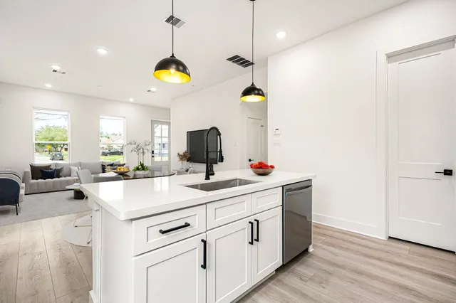 a kitchen with a sink dishwasher and white cabinets with wooden floor