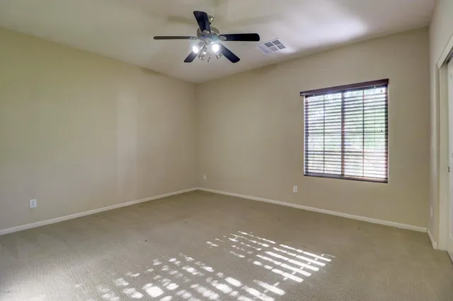 an empty room with a chandelier fan and windows