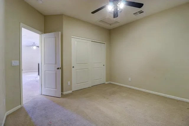 an empty room with chandelier fan and closet area