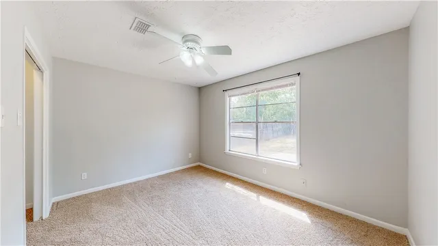 an empty room with chandelier fan and windows