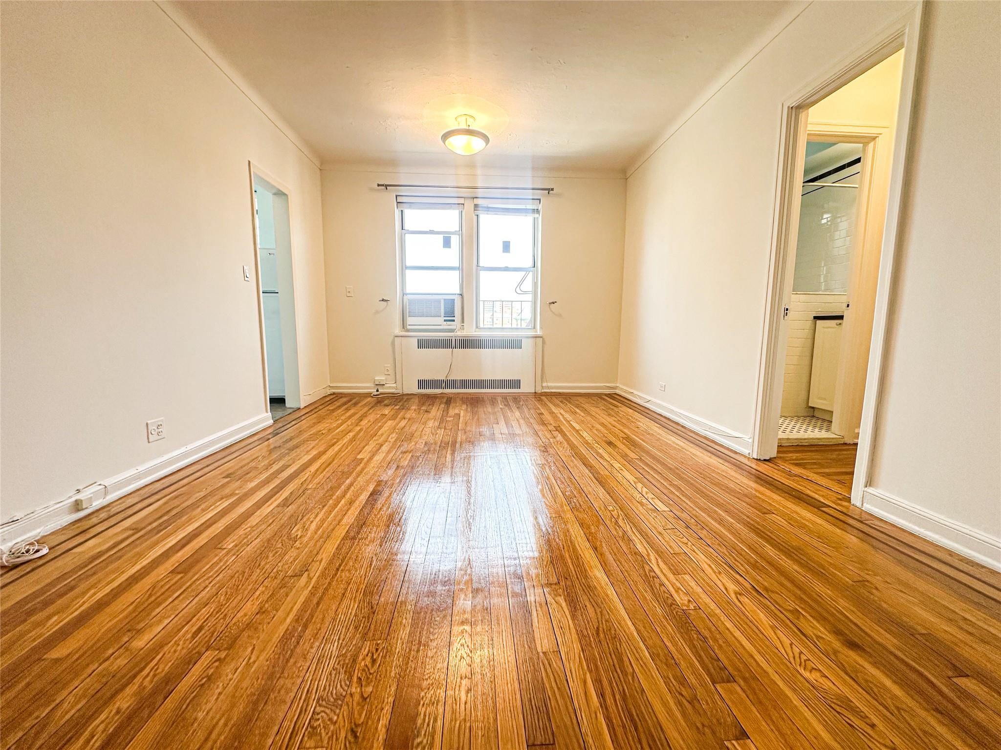 Unfurnished room with crown molding, hardwood / wood-style flooring, baseboards, and radiator heating unit