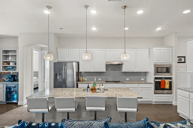 a kitchen with kitchen island granite countertop a refrigerator a stove a sink and a dining table with wooden floor