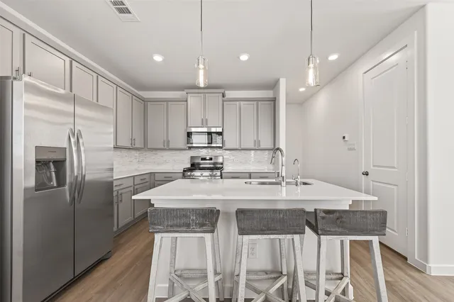 a kitchen with stainless steel appliances granite countertop a sink a stove a refrigerator and island with wooden floor