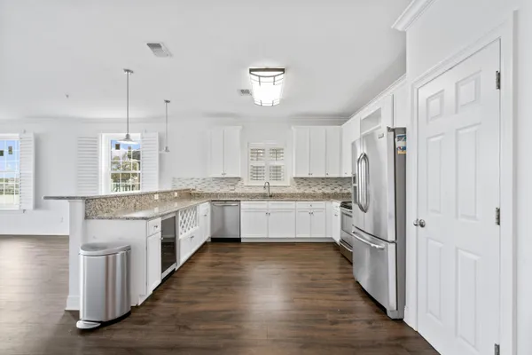 a large kitchen with granite countertop a refrigerator a oven a sink and white cabinets with wooden floor