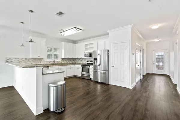 a large white kitchen with granite countertop a stove top oven a sink dishwasher a refrigerator and white cabinets with wooden floor