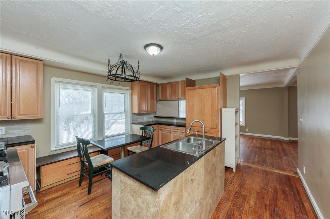 5062 Lee Road Maple Heights, OH 44137 - Photo 8 of 50 Kitchen with an island with sink, backsplash, a textured ceiling, dark wood-style floors, and a chandelier