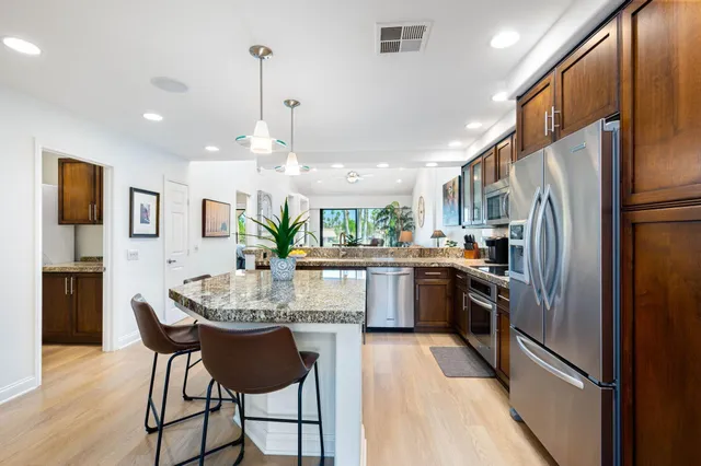 a kitchen with stainless steel appliances granite countertop a refrigerator a stove a sink dishwasher a dining table and chairs with wooden floor