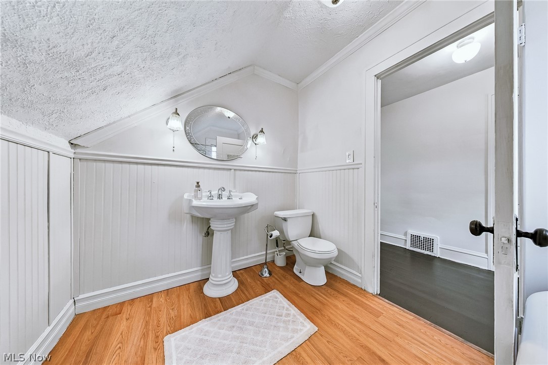 24958 Kennedy Ridge Road North Olmsted, OH 44070 - Photo 31 of 43 Pedestal sink with chrome fixtures, oval mirror with sconce lighting, white wainscoting, wood-finish flooring, and sloped ceiling