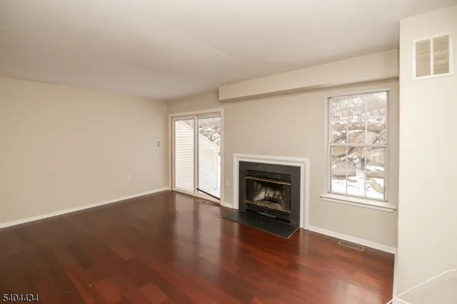 an empty room with wooden floor fireplace and windows