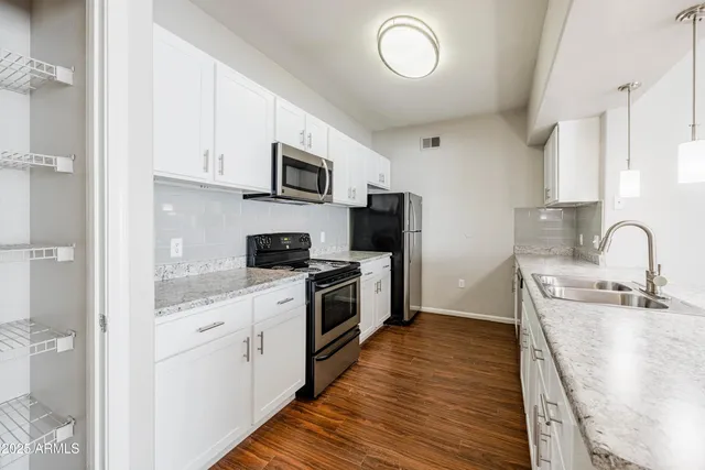 a kitchen with stainless steel appliances granite countertop a sink a stove top oven a refrigerator with white cabinets and wooden floor