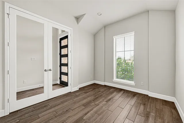 an empty room with wooden floor closet and windows