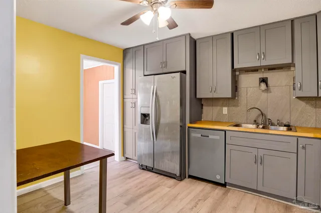 a kitchen with stainless steel appliances granite countertop a refrigerator a sink dishwasher and white cabinets with wooden floor