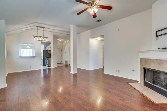 an empty room with wooden floor a chandelier fan and a fireplace