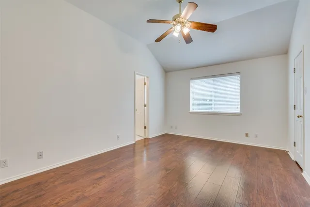 an empty room with wooden floor chandelier fan and windows