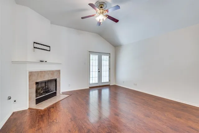 a view of an empty room with wooden floor fireplace and a window
