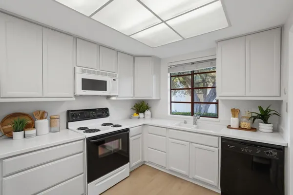 a kitchen with white cabinets appliances a sink and a window