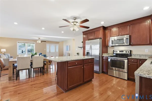 a large kitchen with stainless steel appliances granite countertop a stove refrigerator and a dining table with wooden floor