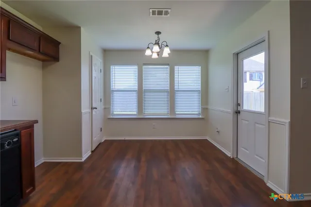 an empty room with wooden floor chandelier and windows