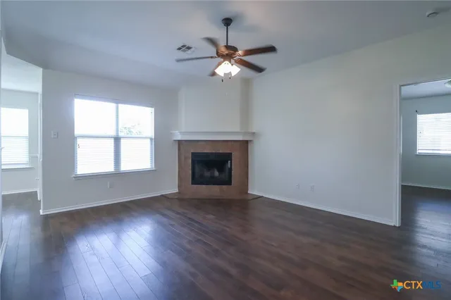 an empty room with wooden floor a chandelier fan and windows