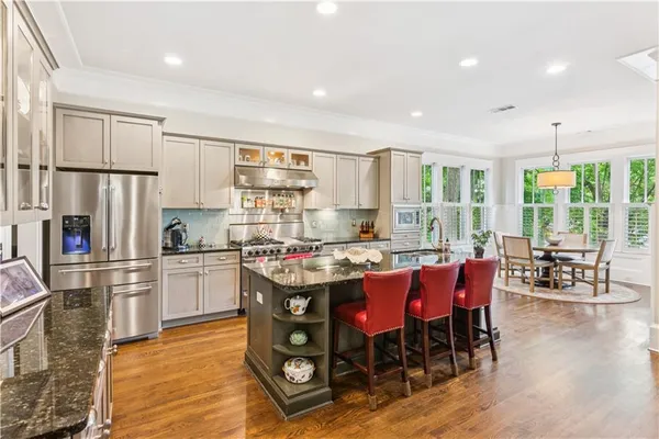 a kitchen with stainless steel appliances granite countertop a stove a refrigerator a kitchen island a dining table and chairs with wooden floor