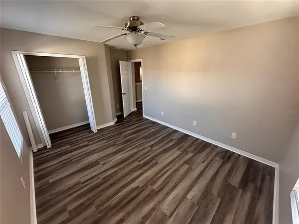 a view of an empty room with wooden floor and a ceiling fan