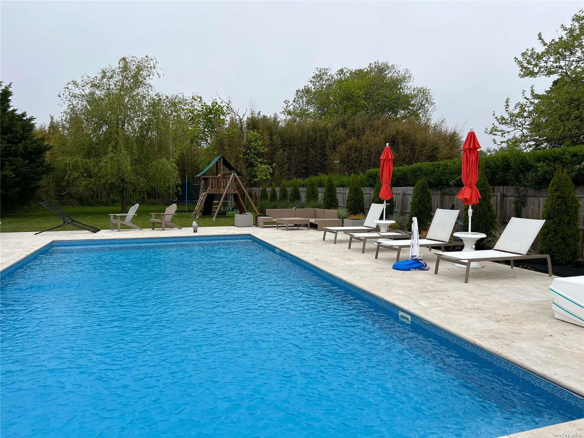 66 Library Avenue Westhampton Beach, NY 11978 - Photo 1 of 26 a swimming pool with outdoor seating and trees in the background
