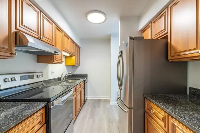 a kitchen with stainless steel appliances granite countertop a refrigerator a stove and a sink with wooden floor