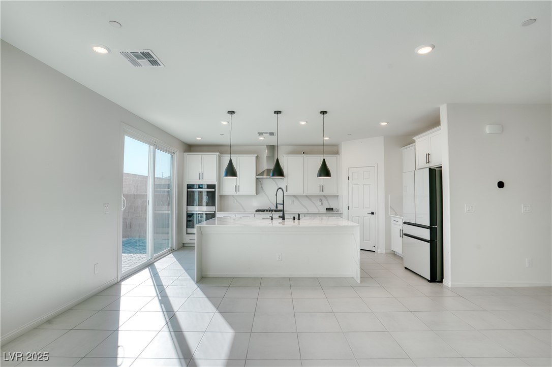 3777 Alla Rocca Avenue Henderson, NV 89044 - Photo 13 of 55 Kitchen with freestanding refrigerator, an island with sink, white cabinets, light stone counters, and stainless steel double oven