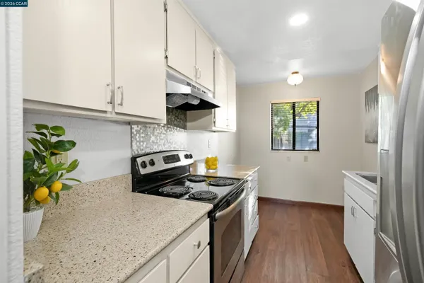 a kitchen with stainless steel appliances a sink a stove white cabinets a dining table and chairs