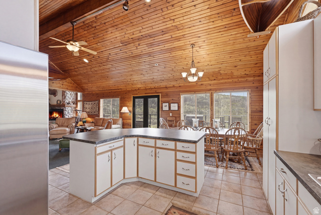 6 Beaver Springs Rancheros Oakley, UT 84055 - Photo 19 of 68 Expansive open-concept living space featuring vaulted wood-paneled ceilings, a central kitchen island with white cabinetry, tile flooring, a dining area with pendant lighting, and a living area with a stone fireplace