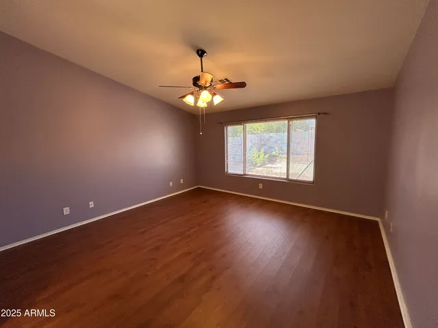 an empty room with wooden floor chandelier fan and windows