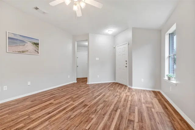 a view of empty room with wooden floor and fan