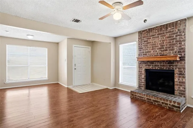 a view of an empty room with wooden floor fireplace and a window