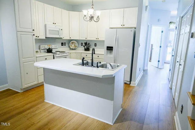 a kitchen with a sink a refrigerator a stove and white cabinets with wooden floor