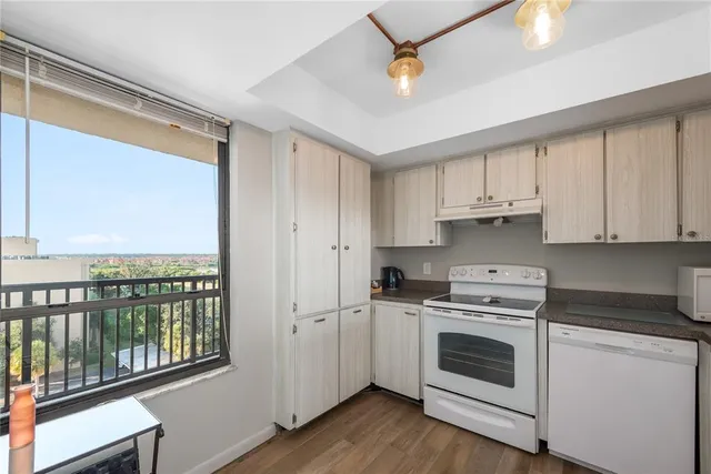 a kitchen with a stove a sink and white cabinets with wooden floor next to windows