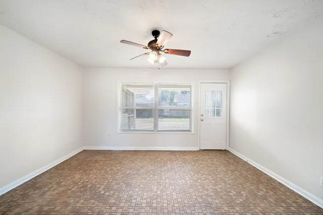 an empty room with chandelier fan and windows