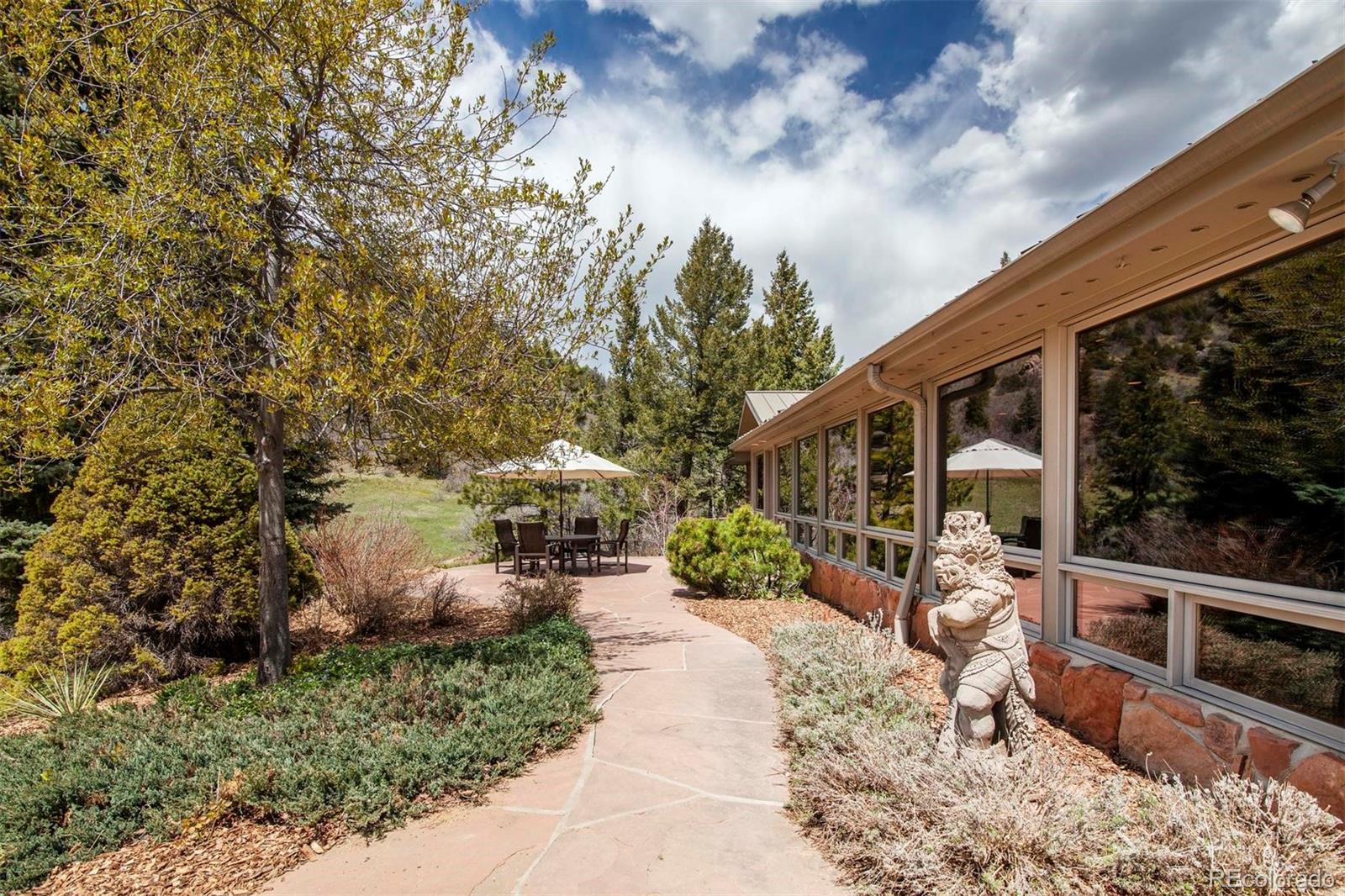 18332 Stone Gate Drive Morrison, CO 80465 - Photo 3 of 40 a view of a patio with table and chairs under an umbrella with large trees