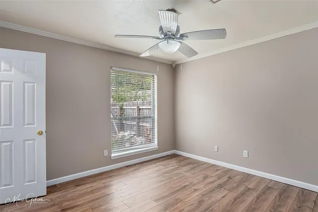 an empty room with wooden floor fan and windows