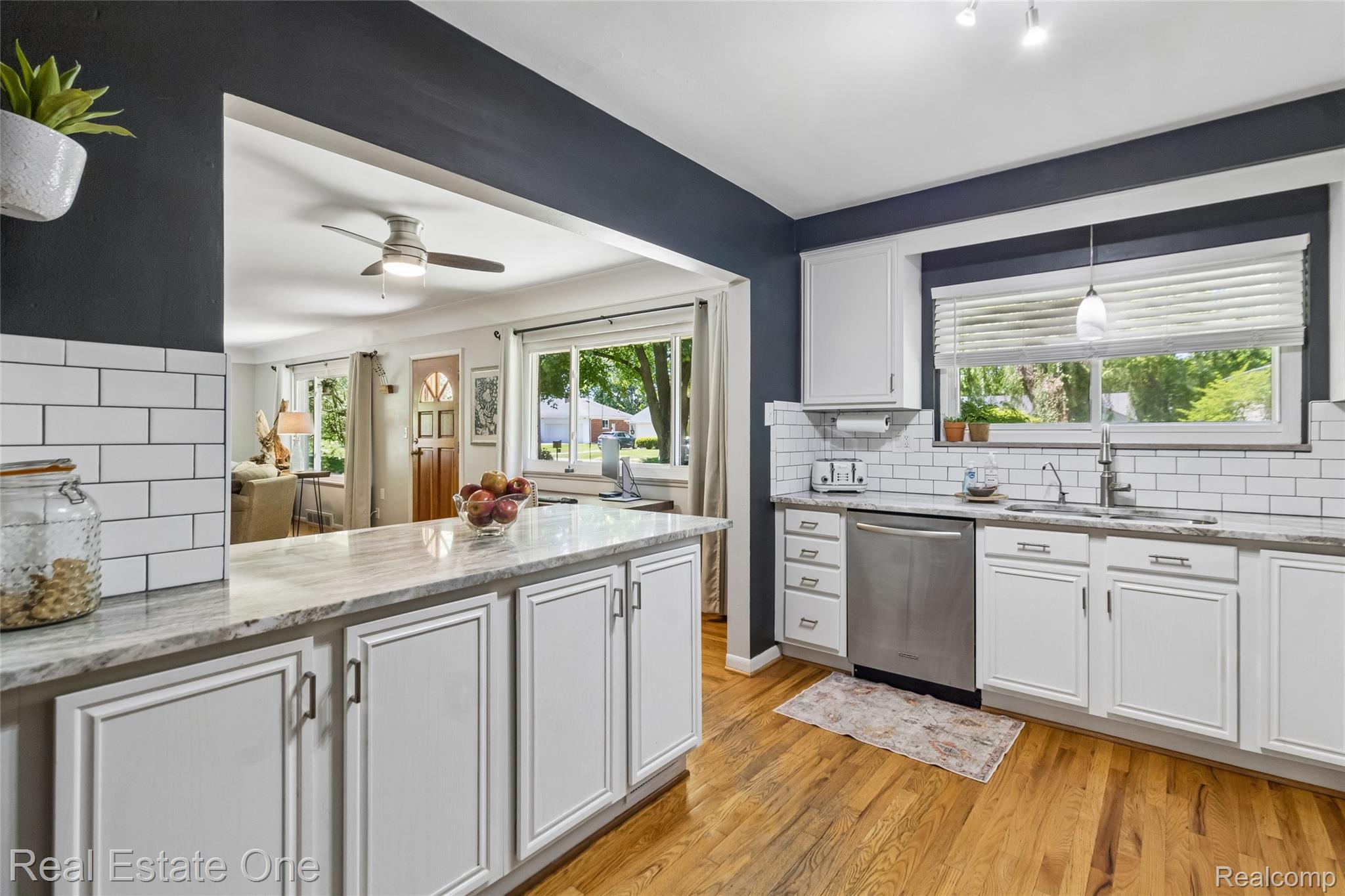 2189 Devonshire Road Bloomfield Hills, MI 48302 - Photo 12 of 50 Kitchen featuring a white subway tile backsplash, white cabinetry, integrated stainless steel dishwasher, and wood-finish flooring