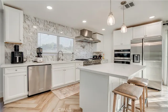 a kitchen with stainless steel appliances kitchen island granite countertop a stove a sink a refrigerator and white cabinets with wooden floor