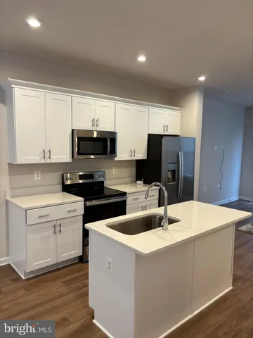 a kitchen with granite countertop a refrigerator a stove a sink and white cabinets with wooden floor