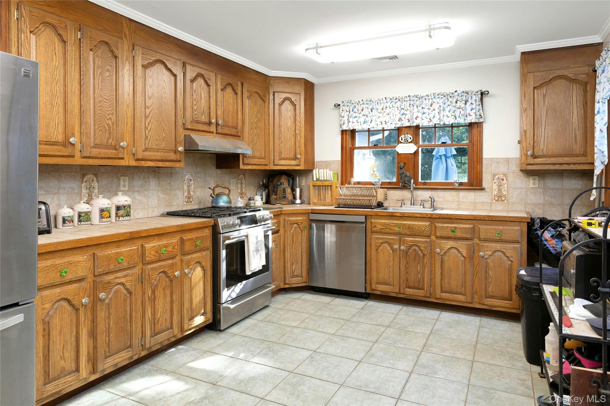 73 Lake Ellis Road Wingdale, NY 12594 - Photo 13 of 41 Kitchen featuring brown cabinets, stainless steel appliances, decorative backsplash, light tile patterned floors, and ornamental molding